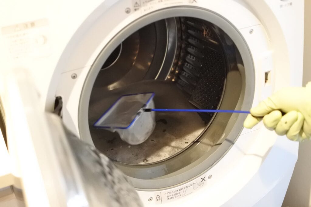 網を使ってドラム式洗濯機内部に浮いた汚れをすくう様子